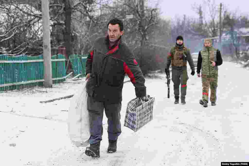 Житель идет по улице на окраине Авдеевки, за ним — российские военные. 19 февраля 2024 года. Когда в феврале российские войска приблизились к Авдеевке, остававшиеся в городе жители бежали. Неясно, сколько человек решили остаться 