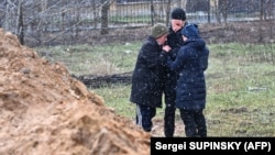Oameni în apropierea unei gropi comune descoperite în localitatea Bucea de lângă Kiev.