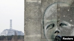 Ýüzün surat çekilen diwaryň arkasynda Çernobyl atom elektrik stansiýasyndaky 4-nji reaktoryň üstüni örtýän sarkofag görünýär, 4-nji aprel.