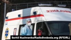 Медик у захисному костюмі біля машини швидкої допомоги
